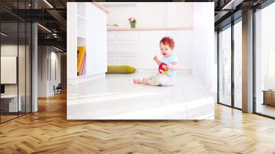 cute ginger baby boy playing with toys in bright kitchen, at home Wall mural