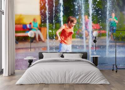 excited boy having fun between water jets, in fountain. Summer in the city Wall mural