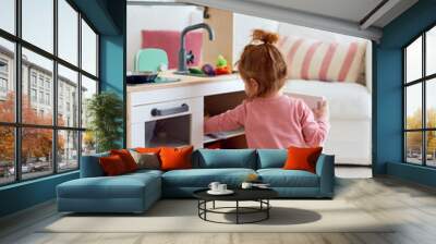 toddler baby girl playing on toy kitchen at home Wall mural