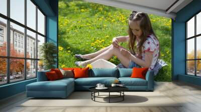 Little girl on dandelion lawn gathering dandelion Wall mural