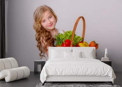 a blonde girl with a basket of fresh vegetables smiles on a gray background, a healthy food concept for children Wall mural