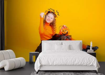 a teenage girl in a witch costume on a yellow background, holding a confent pumpkin eating marmalade worms halloween party Wall mural