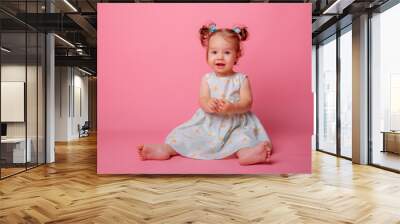 baby girl in a beautiful dress sitting on a pink background Wall mural