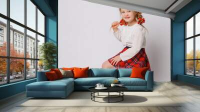 child girl in school uniform sitting on a stack of books isolated on a white background Wall mural