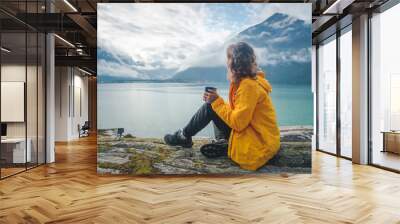 A young beautiful girl is drinking tea on the shore of the fjord, a trip to Norway, the Nordic beauty Wall mural