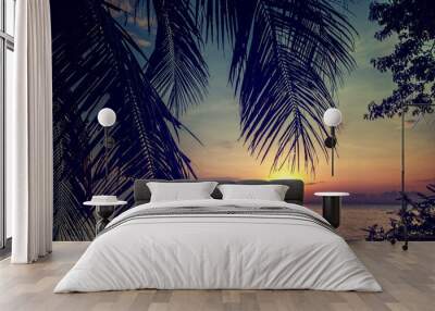 Beautiful bright tropical sunset on the seashore, view of the sky and water through the silhouette of a palm tree Wall mural