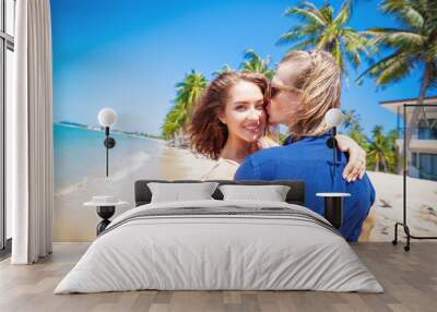 Beautiful happy girl in the arms of a guy on bright tropical beach, vacation honeymoon Wall mural