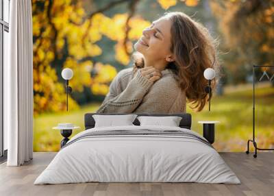 Beautiful smiling caucasian young adult woman in a beige sweater enjoying nature and fresh air walking in the autumn park Wall mural