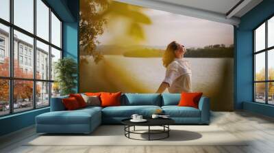 Beautiful young relaxed woman in white blouse enjoying nature breathing fresh air meditating on the river on an autumn day Wall mural