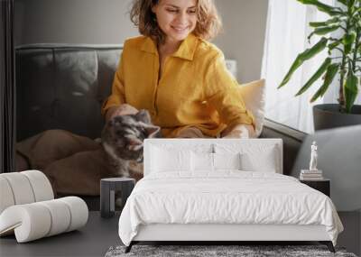 Casual woman in yellow shirt working on laptop with her cat on sofa, sitting together in modern room with window ang green plan Wall mural