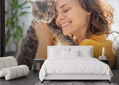 Close-up portrait of a beautiful cheerful young woman with a cute gray cat in her arms at home Wall mural