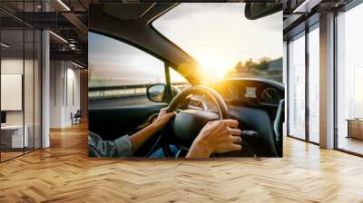 Female hands on the steering wheel of a car. Woman driving a car at sunset on the seashore. Auto travel concept Wall mural