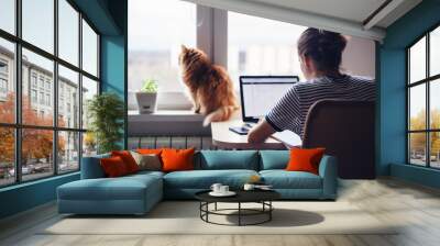 Girl student freelancer working at home on a task, the cat is sitting on the window Wall mural