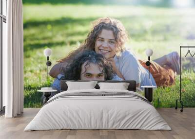 Happy young curly couple lying on the green grass in the summer sunny park Wall mural