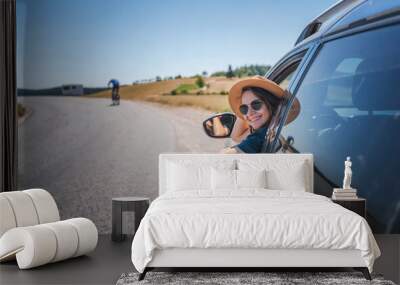 Happy young woman driver traveler in hat and sunglasses sitting behind the wheel of car on summer country road Wall mural