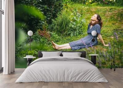 Happy young woman in dress relaxing and enjoying summer while sitting on green grass in her garden Wall mural