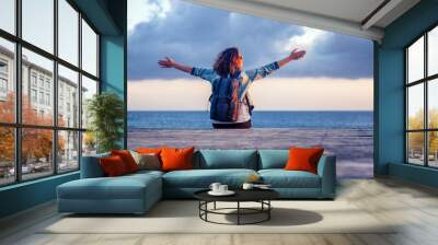 portrait of a beautiful happy young woman sitting on a wooden pier on the background of the sea and a beautiful sunset and admiring the scenery Wall mural