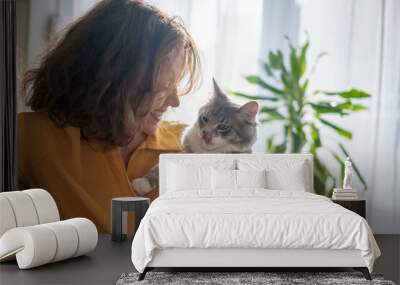 Portrait of a young beautiful woman in a yellow shirt hugging with a gray fluffy cat while sitting on sofa Wall mural