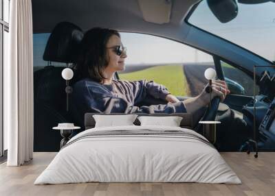 Portrait of an adult young caucasian woman in sunglasses driving a car. Agricultural fields outside the car window Wall mural