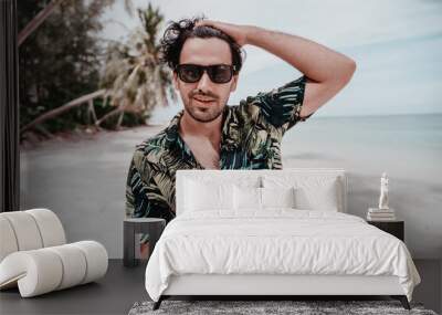 Portrait of sexy latino guy brunet man in hawaiian shirt and sunglasses on tropical beach. Men's fashion and beauty in travel and vacation Wall mural