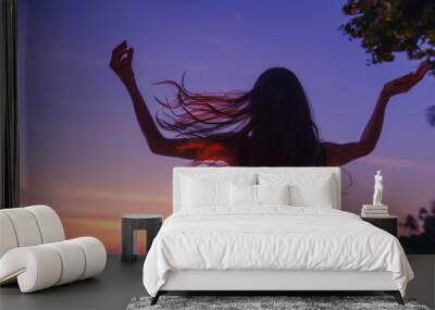 Silhouette of a beautiful slim young woman on a background of bright colorful sunset on a tropical beach Wall mural