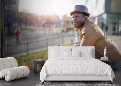 Stylish happy young african american man in hat and yellow jacket on city streets Wall mural