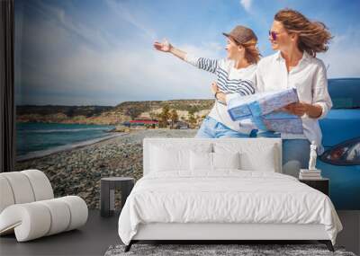 Two young beautiful girls girlfriends traveling together in a car, on the beach on a bright sunny summer day, with map in hand, travel and holidays Wall mural