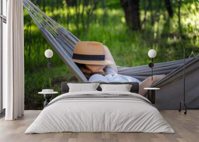 Woman resting in a hammock in a summer garden covering her face with a straw hat. Summer relax vacation Wall mural