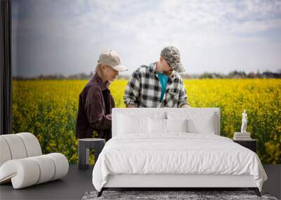 Young adult caucasian couple of farmers standing in a spring flowering canola field checking the quality of seedlings Wall mural