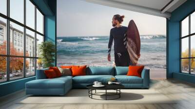 Young attractive sporty stylish man with a surfboard in his hands against the background of the ocean beach,sport freedom vacation travel concept Wall mural