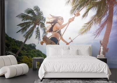 Young beautiful happy woman in top and shorts swinging on a swing on the shore of a tropical sea during vacation. Travel and vacation concept Wall mural