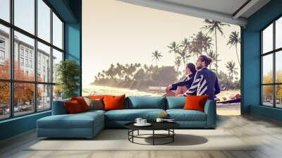 Young beautiful loving couple friends are sitting on the sand by the ocean with surfboards and watching sports active lifestyle holidays honeymoon... Wall mural