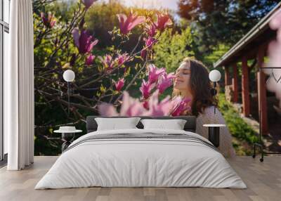 Young beautiful woman enjoying the spring of her home in the garden near a blooming magnolia tree inhaling the aroma of flowers Wall mural