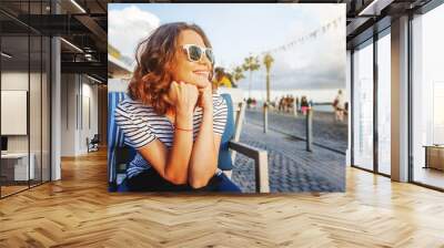 young beautiful woman girl in a striped T-shirt sitting in a street cafe smiling, seaside town, vacation and travel Wall mural