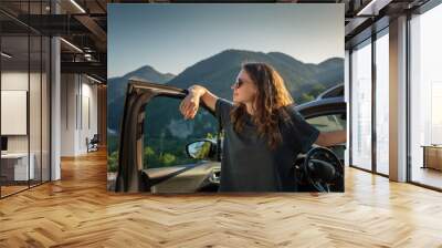 Young beautiful woman traveling by car in the mountains, summer vacation and adventure Wall mural