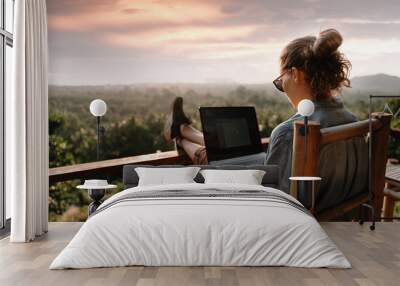 Young business woman working at the computer in cafe on the rock. Young girl downshifter working at a laptop at sunset or sunrise on the top of the mountain to the sea, working day. Wall mural