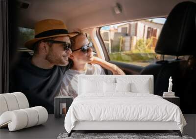 Young cheerful happy couple of travelers sitting in the car in the back seat looking out the window Wall mural