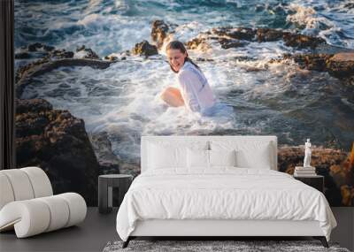 Young cheerful relaxed woman in a white shirt in a natural sea bath on the seashore. Thalassotherapy wellness concept Wall mural