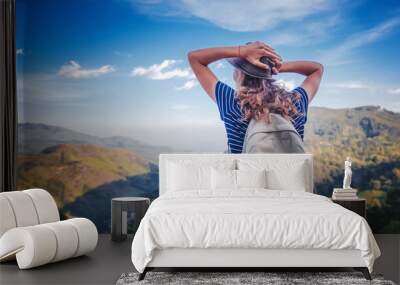 Young female traveler with a backpack and in a hat admiring enjoying the beautiful mountain landscape, travel and freedom lifestyle Wall mural