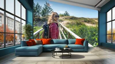 Young happy beautiful girl walks along the cold shore of the Baltic Sea in windy sunny weather, traveling to the Scandinavian countries Wall mural