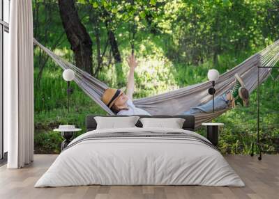 Young happy caucasian woman in a hat lying in a hammock in a green garden enjoying a summer day Wall mural