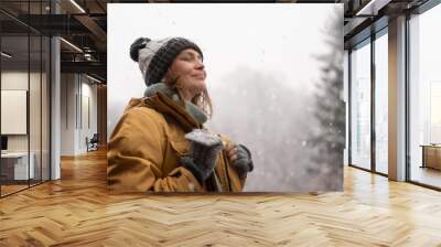 Young mature adult caucasian woman in a hat and yellow jacket breathing fresh air in the winter forest Wall mural