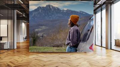 Young woman traveler standing near car watching a beautiful mountain view while travel driving road trip on vacation Wall mural