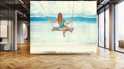 Young woman with long blond hair swinging on a swing on the shore of the tropical sea Wall mural