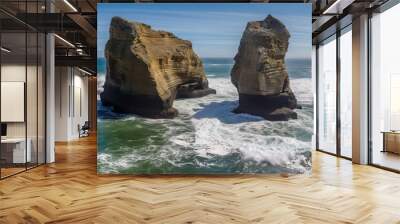  two large rocks sticking out of the ocean next to each other on a sunny day with a blue sky and some waves crashing in front of them.  generative ai Wall mural