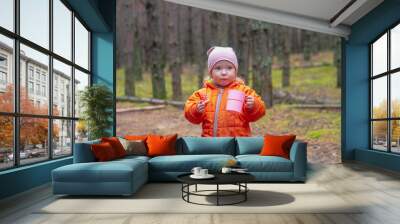 A child girl caucasian 2 years old drinks tea in a pine forest from a mug in autumn Wall mural