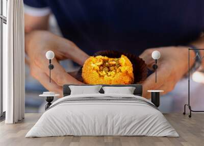 A man eating arancini, italian rice ball al ragu or al sugo, that is stuffed  with meat, peas and tomato sauce and spices, coated with breadcrumbs and deep fried. Sicilian street food, cuisine. Wall mural