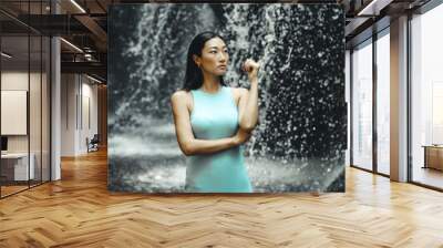 Attractive Asian woman posing near the waterfall. Water splashing. Nature and environment. Travel lifestyle. Slim woman wearing light blue dress. Copy space. Yeh Bulan waterfall in Bali Wall mural