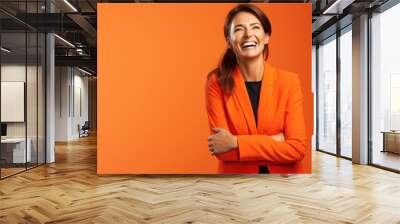 Confident satisfied woman wearing orange official style suit standing and laughs Wall mural