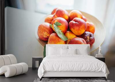 Fresh ripe peaches with leaves on a wooden plate on a kitchen table against the window. Organic food concept and prevention of vitamin deficiency. Fruits for cooking. Wall mural